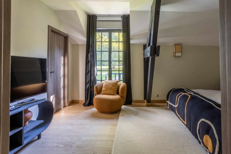 Chambre avec poutre sombre et fauteuil dans une maison de caractère près de Deauville