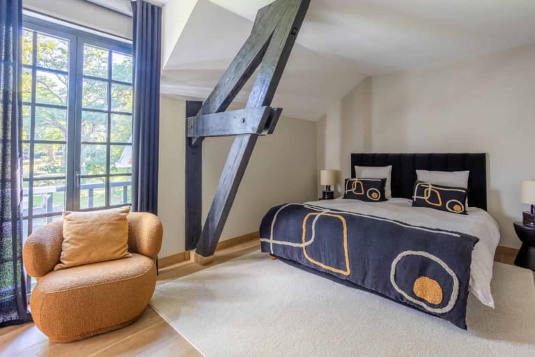 Chambre parentale avec charpente apparente et fenêtres sur le parc